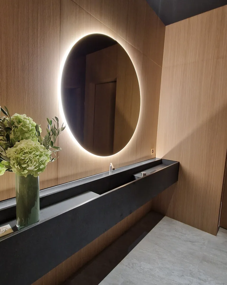 Salle de bains avec miroir rond lumineux, vasque et finitions bois